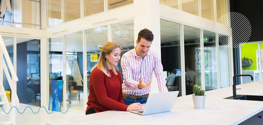 Business-agility-pillar_barriers_two_professionals_talking Two colleagues in discussion while viewing a laptop and seated in a modern office lounge